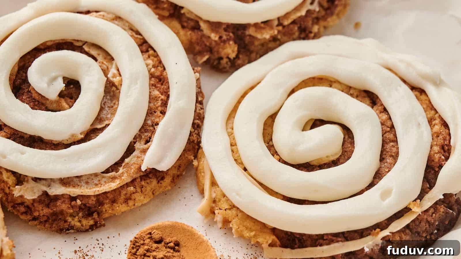 31 Cozy Cinnamon Recipes to Warm Your Home and Soul 10 A delectable close-up of Copycat Crumbl Cinnamon Swirl Cookies, adorned with spiral white icing on a parchment paper background.