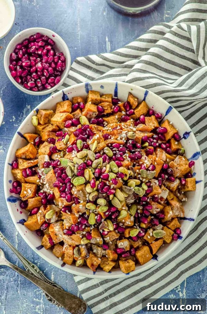 Close up Bird's eye view of a bowl filled with roasted sweet potato cubes topped with Tahini, silan, pistachios and pomegrantes
