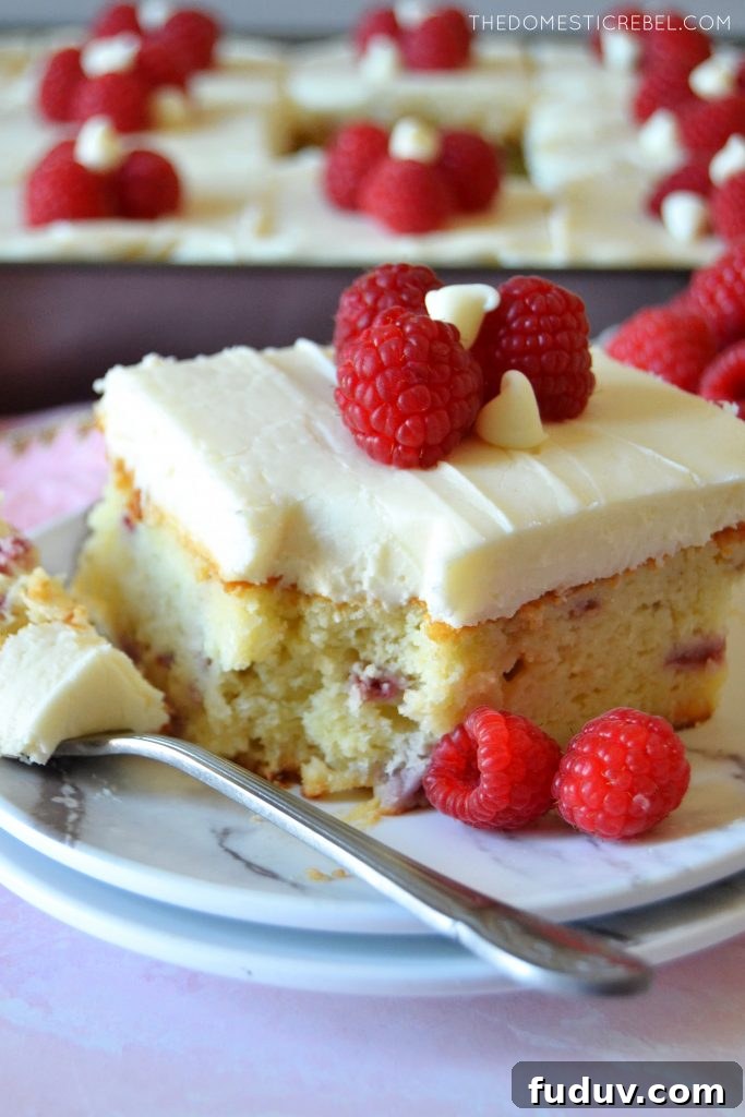 slice of white choc raspberry cake with a bite missing on a white plate