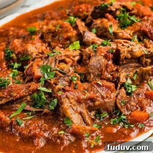 Beef stracotto pot roast in rich tomato sauce garnished with chopped parsley on a white platter.