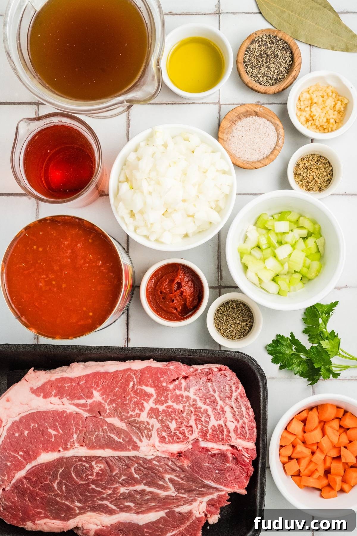 Raw beef, chopped vegetables, spices, tomato sauce, broth, and oil arranged on a white tiled surface.