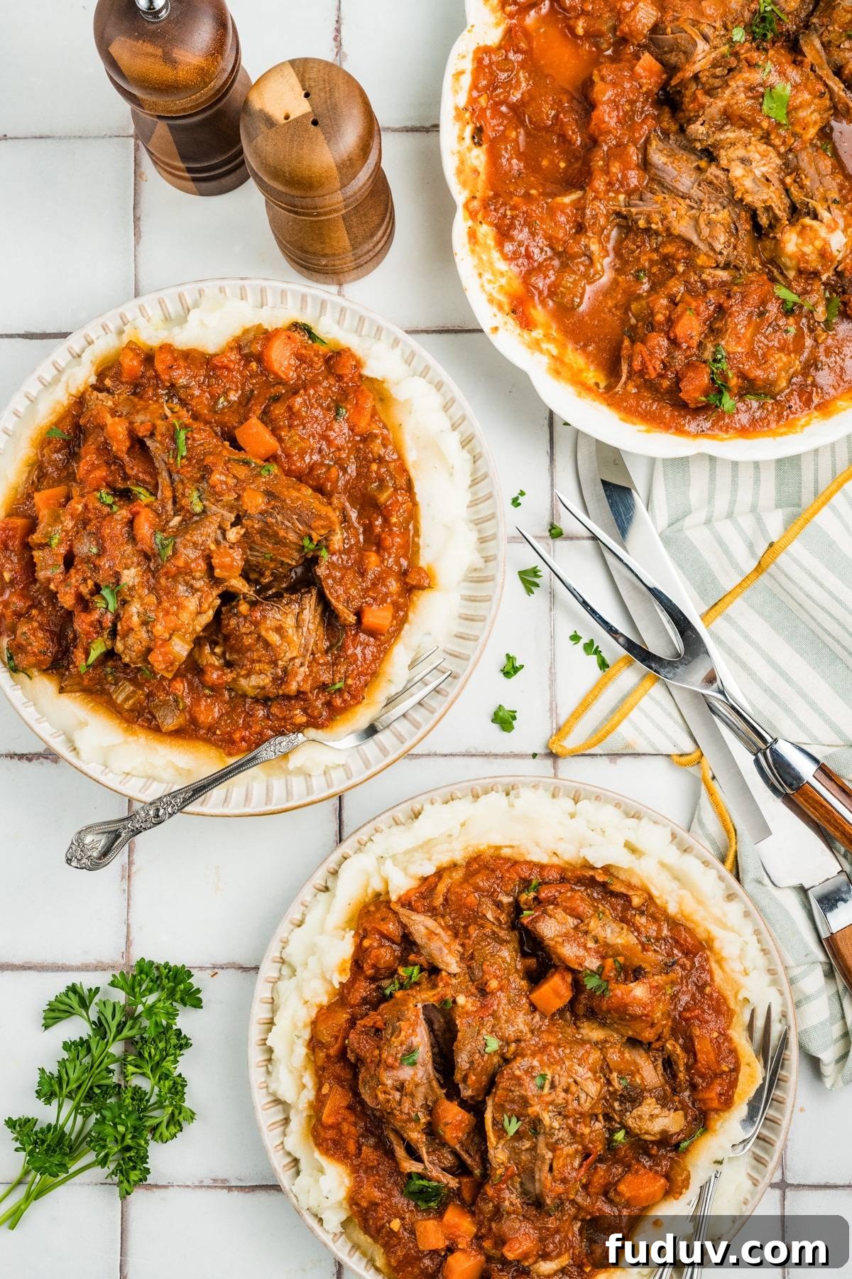 Overhead view of plates with pot roast in tomato sauce, garnished with parsley, on a tiled surface.