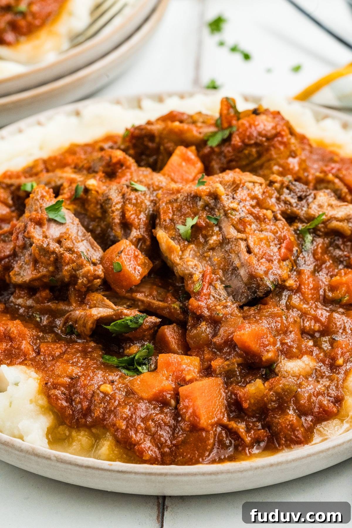 Beef stew with carrots and tomato sauce served over mashed potatoes on a white plate.