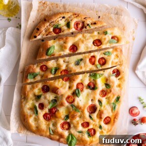A loaf of sourdough Caprese focaccia with a few slices cut into it, drizzled with balsamic
