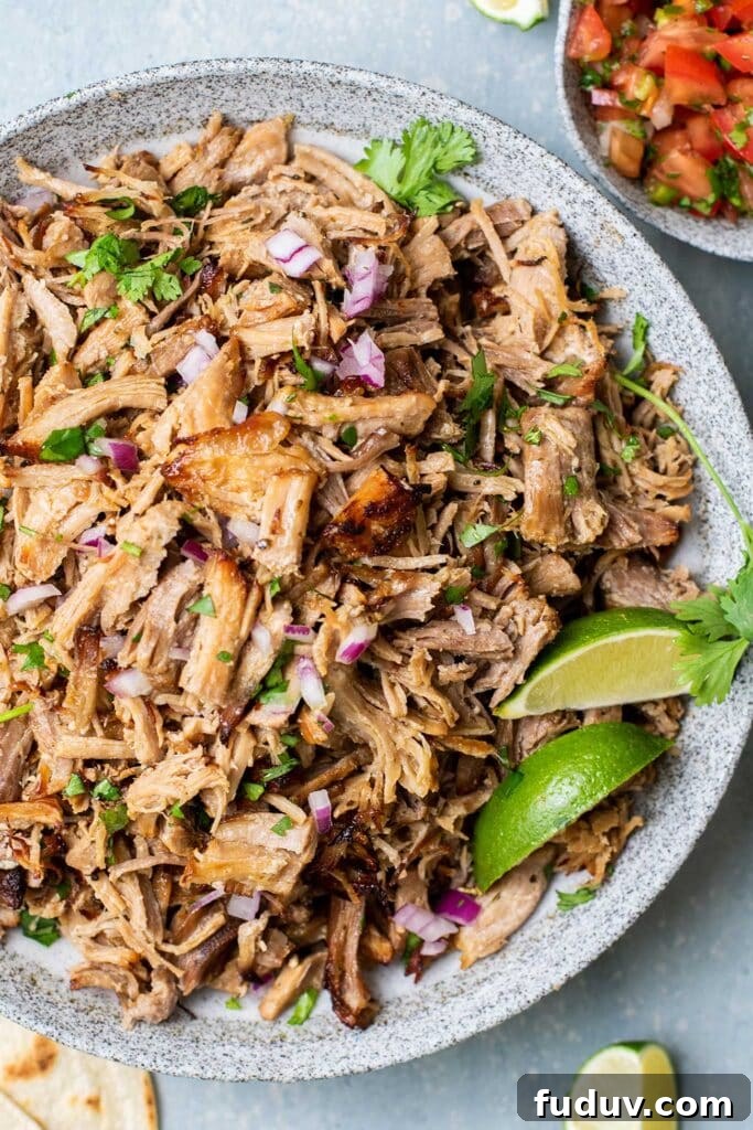 A plate piled high with crispy carnitas, garnished with lime and cilantro.