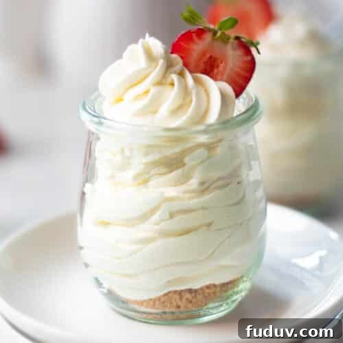 A close-up of cheesecake mousse in a glass jar, topped with whipped cream and a sliced strawberry, showcasing the creamy texture through the glass.