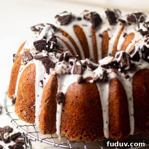 Angled close-up of Oreo pound cake showing thick vanilla glaze dripping over the Bundt ridges and loaded with chunks of crushed Oreos.