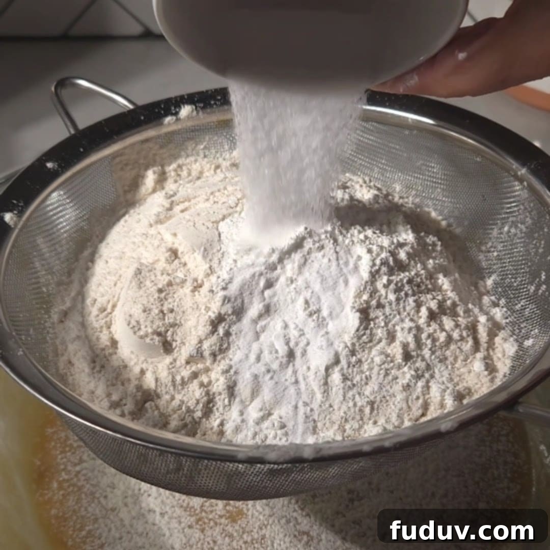 Chewy Chocolate Chip and Gooey Marshmallow Cookies 10 Flour being sifted into a bowl using a mesh strainer, creating a soft pile of dry ingredients for cookie preparation.