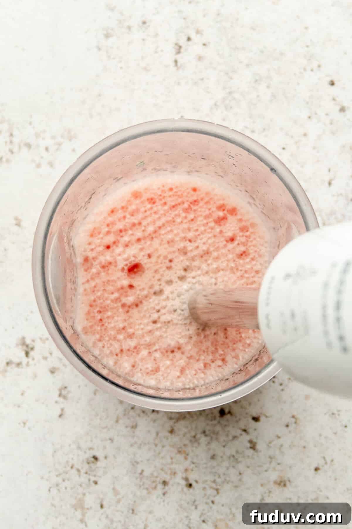 Watermelon and lime juice are blended in a beaker on a light grey surface.