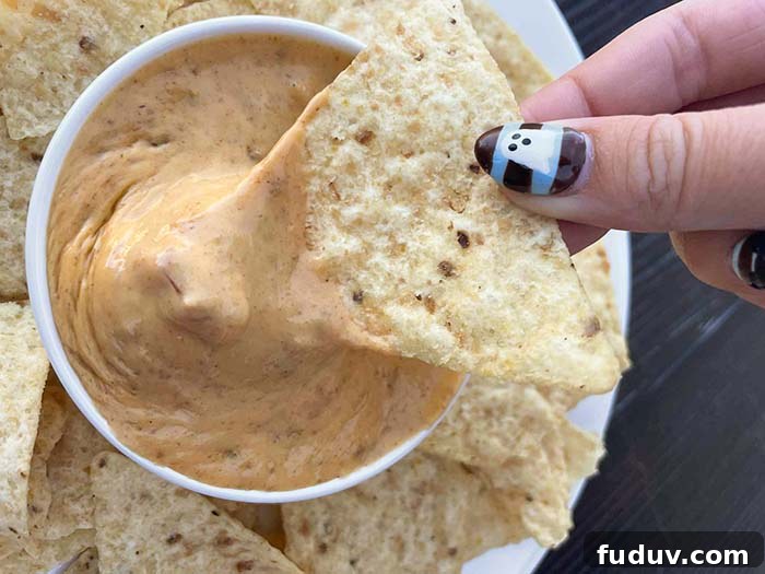 Creamy 3-Ingredient Velveeta Fiesta Dip Recipe 3 A triangle corn chip with fiesta cheese dip held above a small bowl of fiesta cheese dip that is surrounded by corn chips on a large plate.