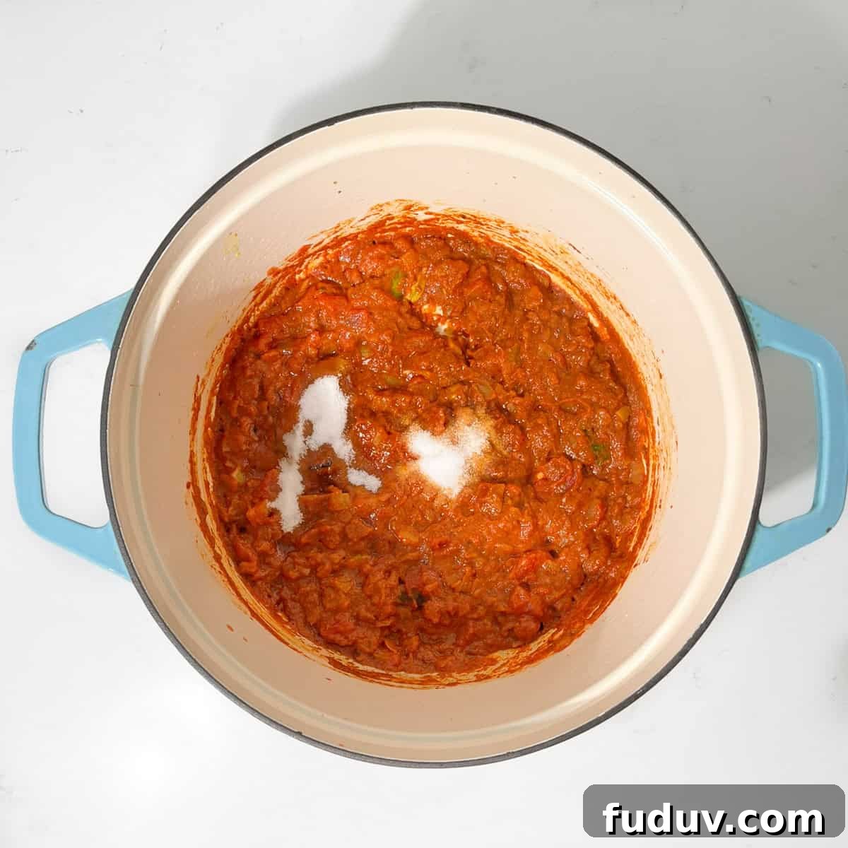 Adding salt and sugar to tomatoes and onions in a large saucepan.
