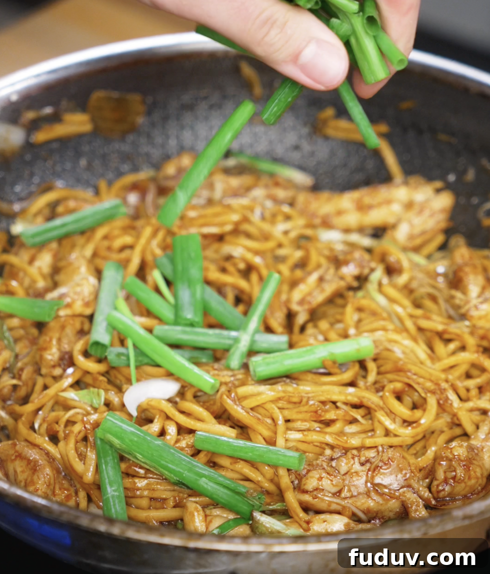 Crispy Chicken Pan-Fried Noodles with Savory Stir-Fry Sauce 9 Fresh scallion greens are being added to the pan as the final touch. They add a pop of color, crunch, and brightness to the finished noodles.