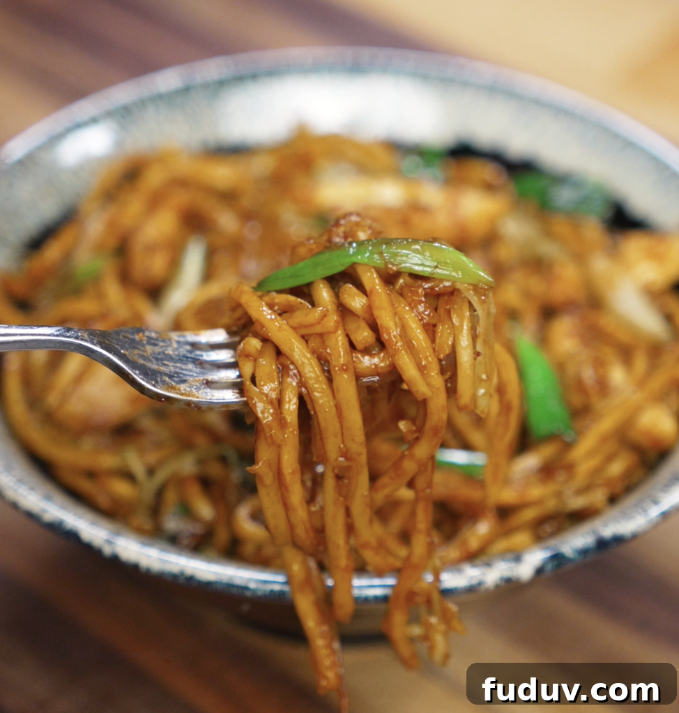 Crispy Chicken Pan-Fried Noodles with Savory Stir-Fry Sauce 3 A fork lifts a glossy bite of pan fried noodles with chicken and scallions from the bowl. The noodles are coated in a rich, savory sauce that clings to every strand.