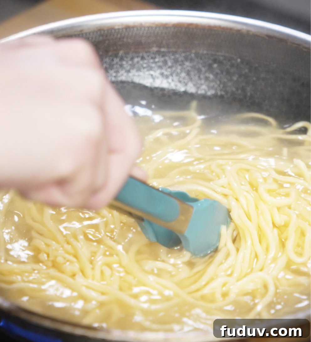Crispy Chicken Pan-Fried Noodles with Savory Stir-Fry Sauce 5 Fresh wheat noodles are boiling in a pot of water, stirred with tongs to prevent sticking. These chewy noodles form the base of the pan-fried dish.