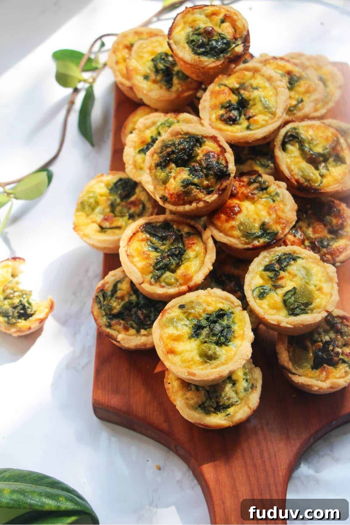 A pile of mini coronation quiches on a small wooden board.
