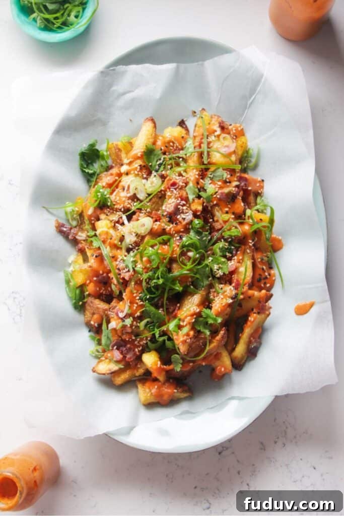 Loaded potato wedges on a large oval white plate with small jug of gochujang bechamel on the side.