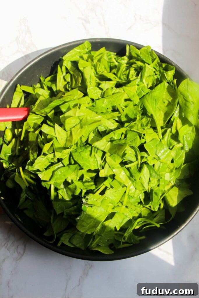 Spinach leaves piled into small frying pan.