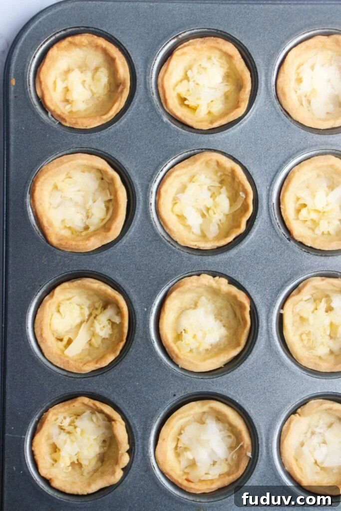 Grated cheese on the base of mini pastry cases in a mini muffin tin.