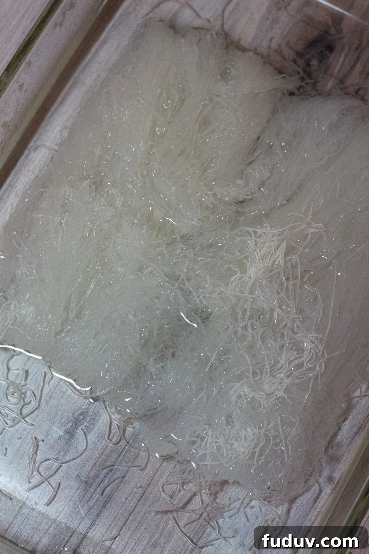 Glass dish with rice noodles soaking in hot water.