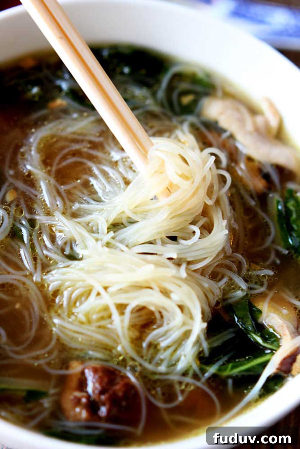 White bowl of Asian Chicken Noodle Soup, rice noodles twirled on chopsticks.
