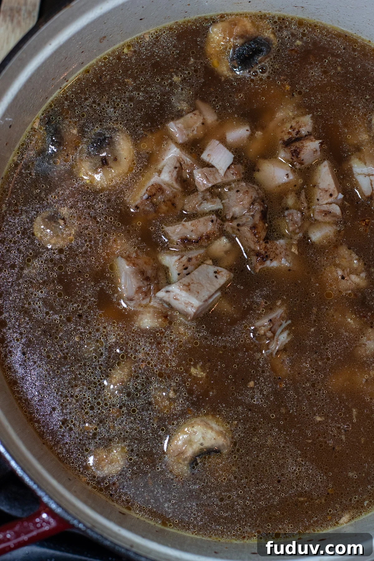 Stock pot filled with chicken noodle soup and mushrooms.