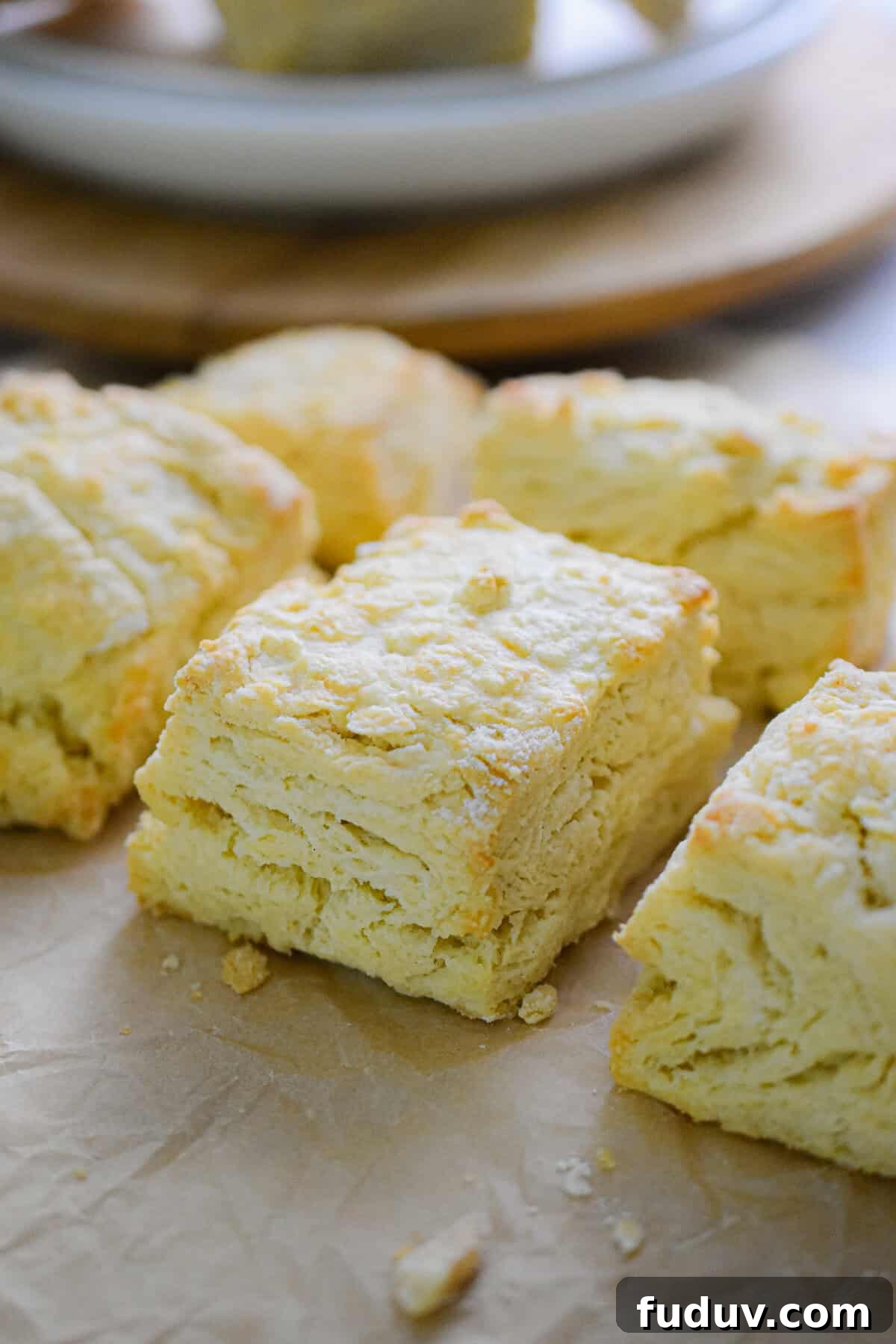 Six biscuits with self rising flour are on a piece of parchment paper with a plate in the background.