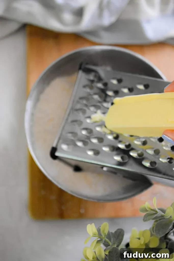 The butter is being grated over a bowl of flour.
