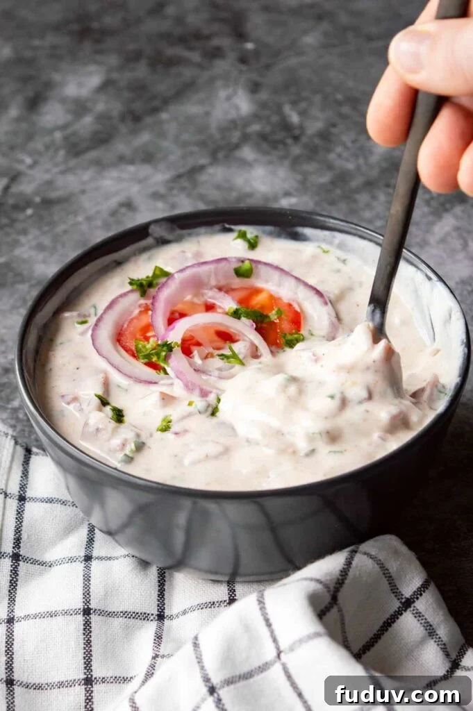 5-Minute Onion Tomato Raita Recipe for Quick Indian Sides 2 A black bowl of white yogurt and onion and tomatoes being stirred.