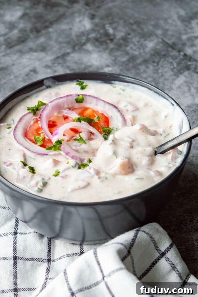 5-Minute Onion Tomato Raita Recipe for Quick Indian Sides 4 A black bowl of chunky raita on a grey background.