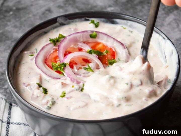 A black bowl of white yogurt and onion and tomatoes being stirred.