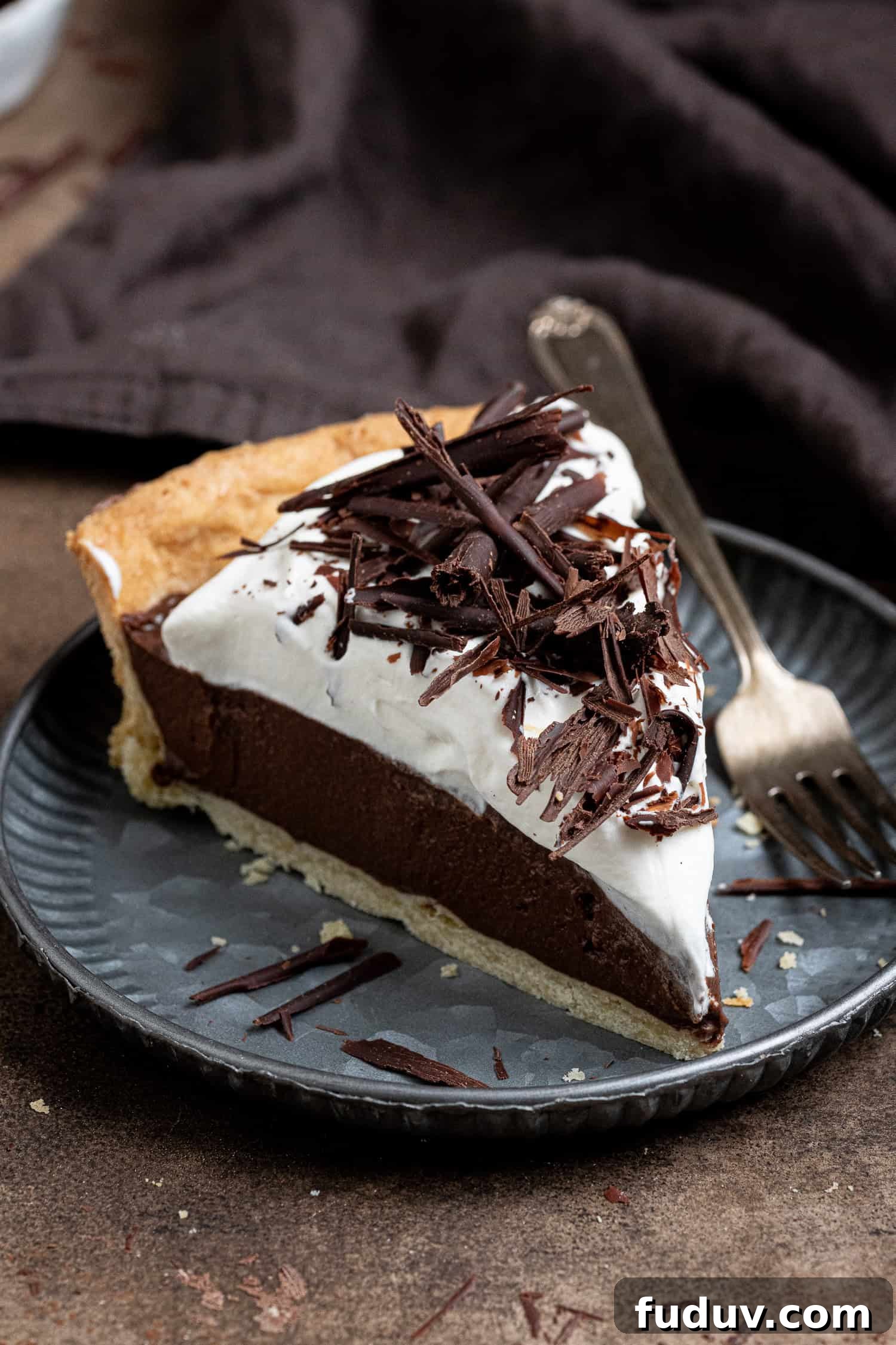 A slice of vegan chocolate cream pie on a metal plate with a fork.