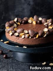 vegan chocolate cheesecake decorated with Easter chocolates on a black cake stand.