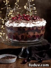 A glass bowl of vegan black forest trifle on a glass cake stand, with fairy lights in the background.
