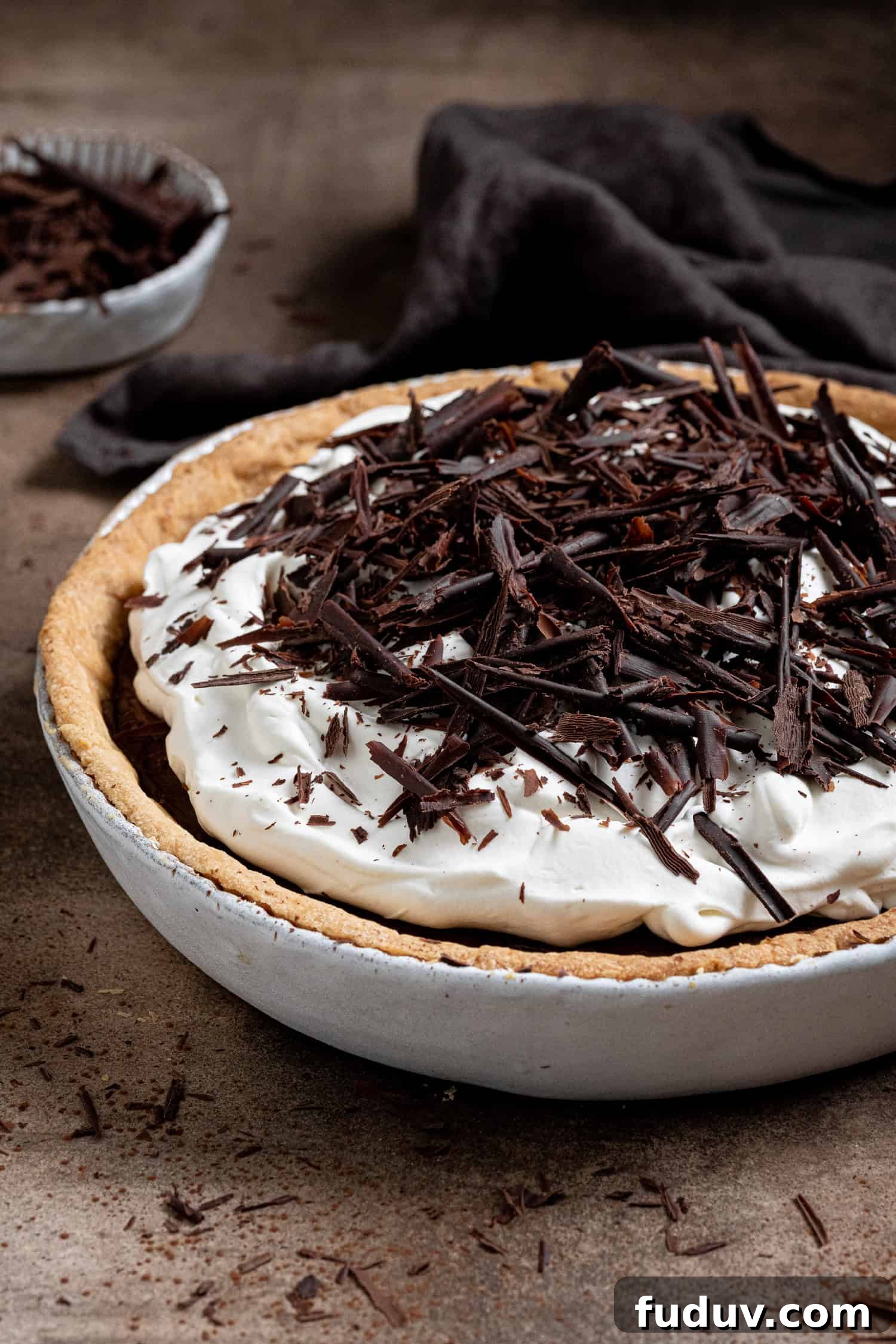 Vegan chocolate cream pie in a ceramic pie dish with a bowl of chocolate shavings.