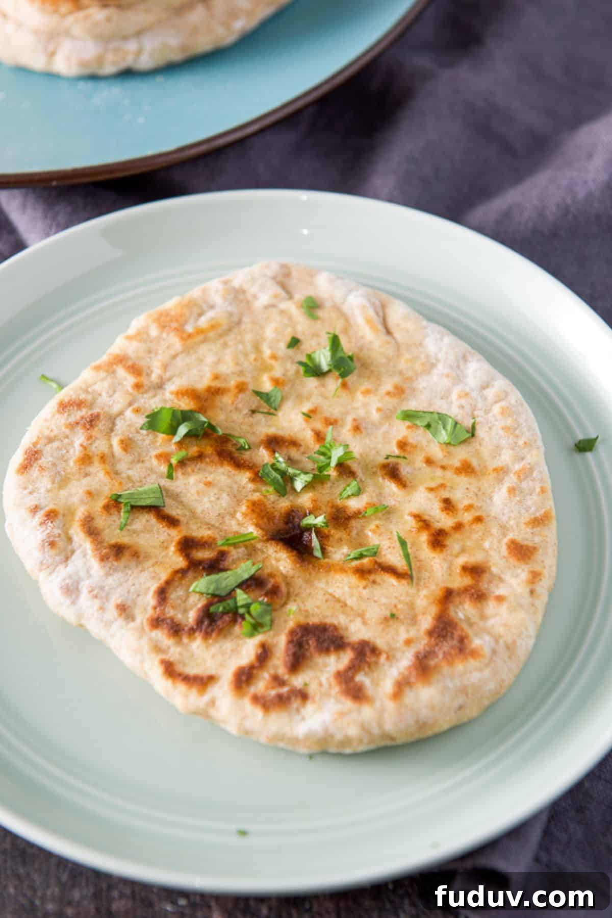 A naan round on a green plate with butter on it and cilantro. There is a pile of bread in the background