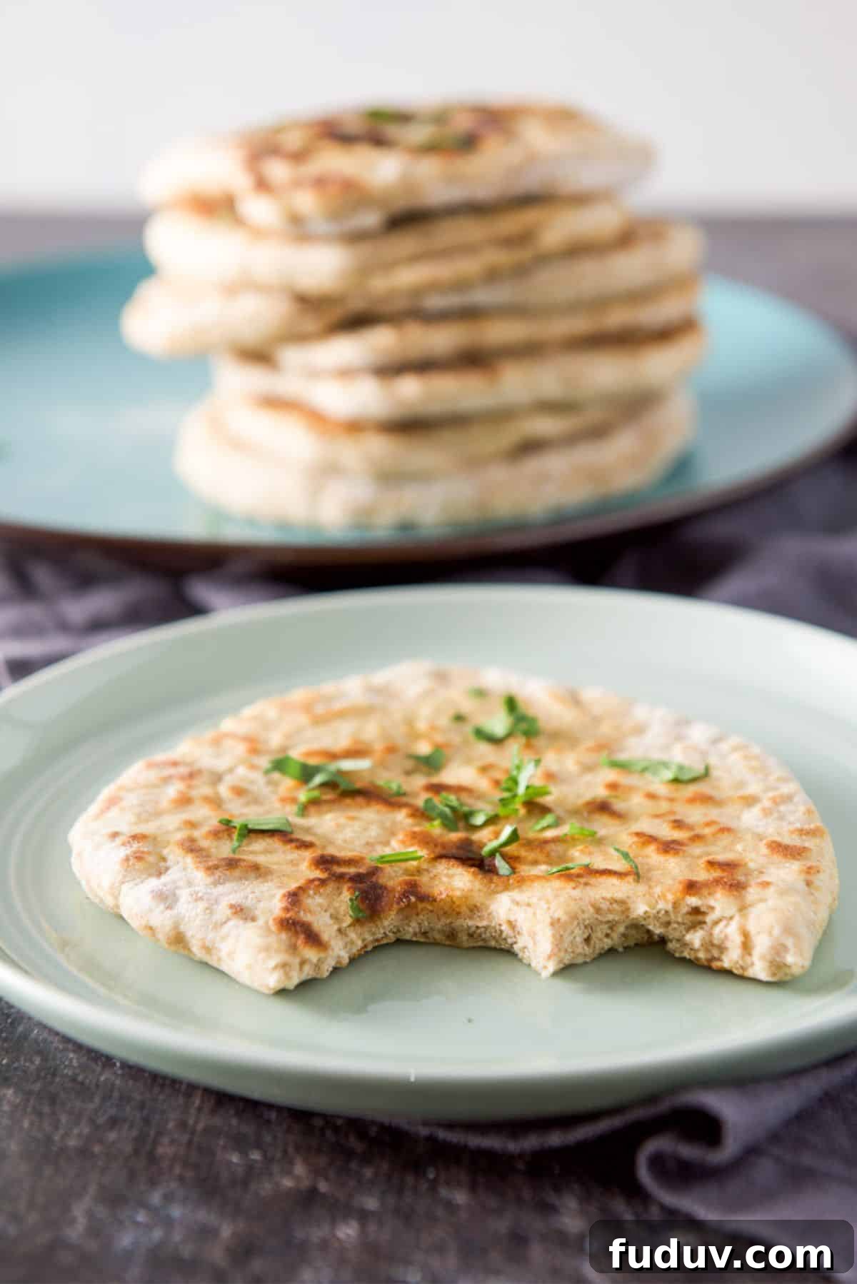 A green plate with a piece of naan on it with two bites out of it. There is a stack of naan in the back