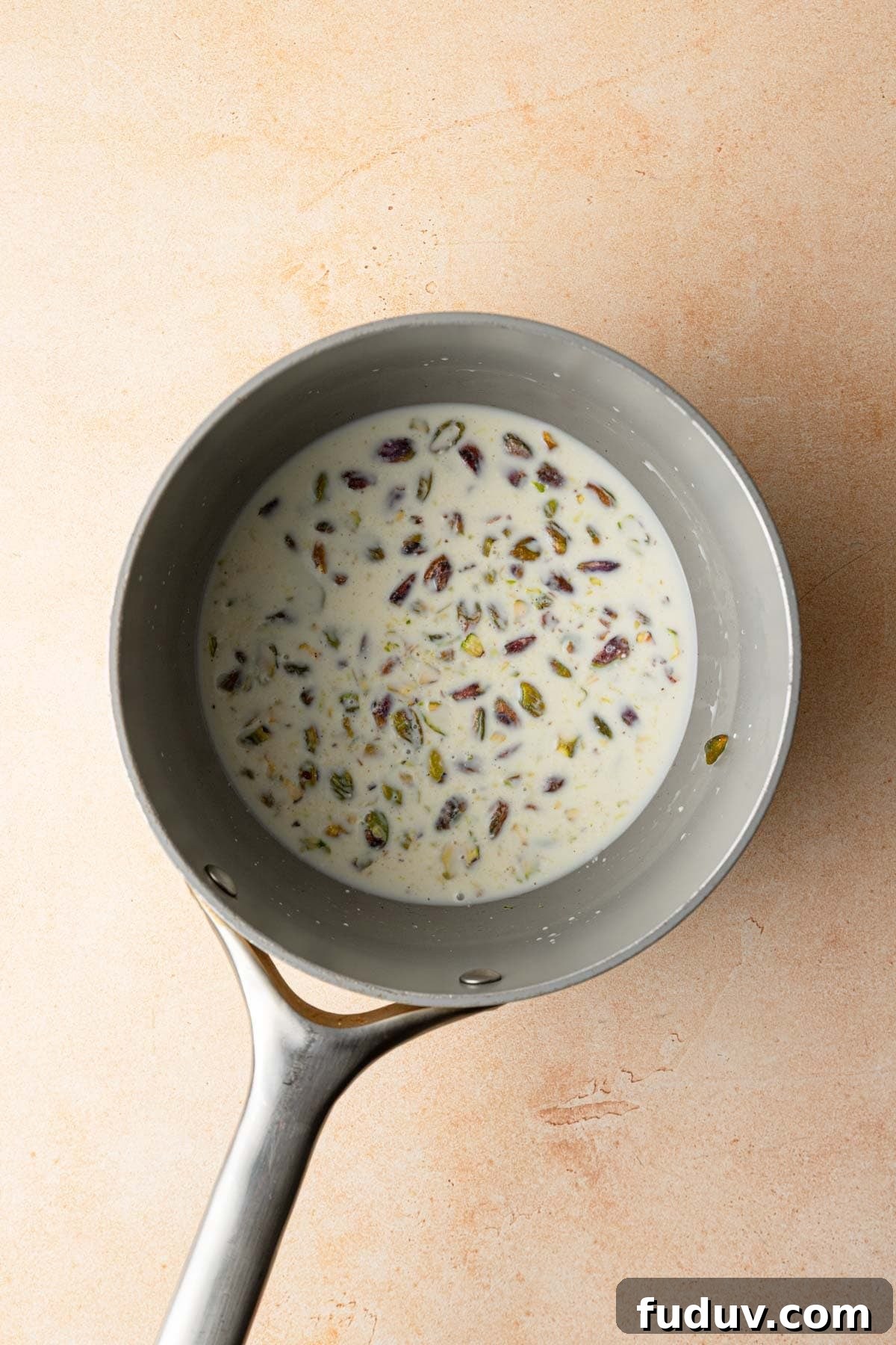 A sauce pan with milk and chopped pistachios.