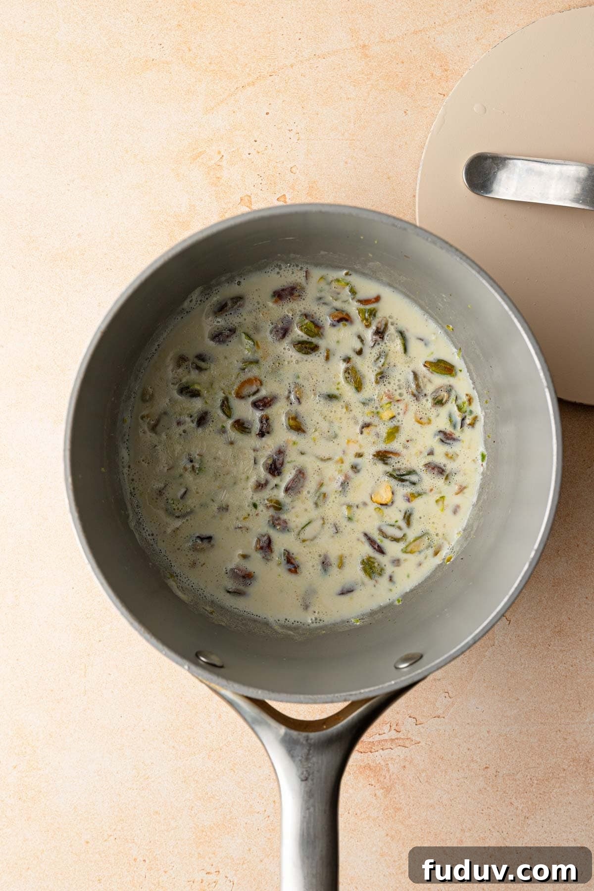 A sauce pan with boiled milk and chopped pistachios, lid next to the pan.