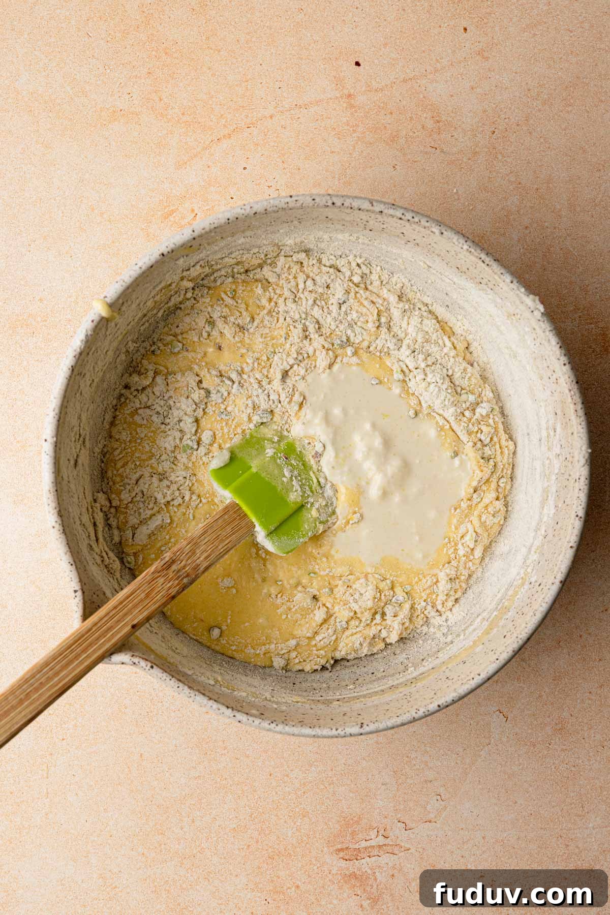 A large bowl raw batter and flour with a rubber spatula.