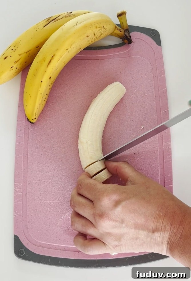 Bananas being chopped into slices on  a pink chopping board.