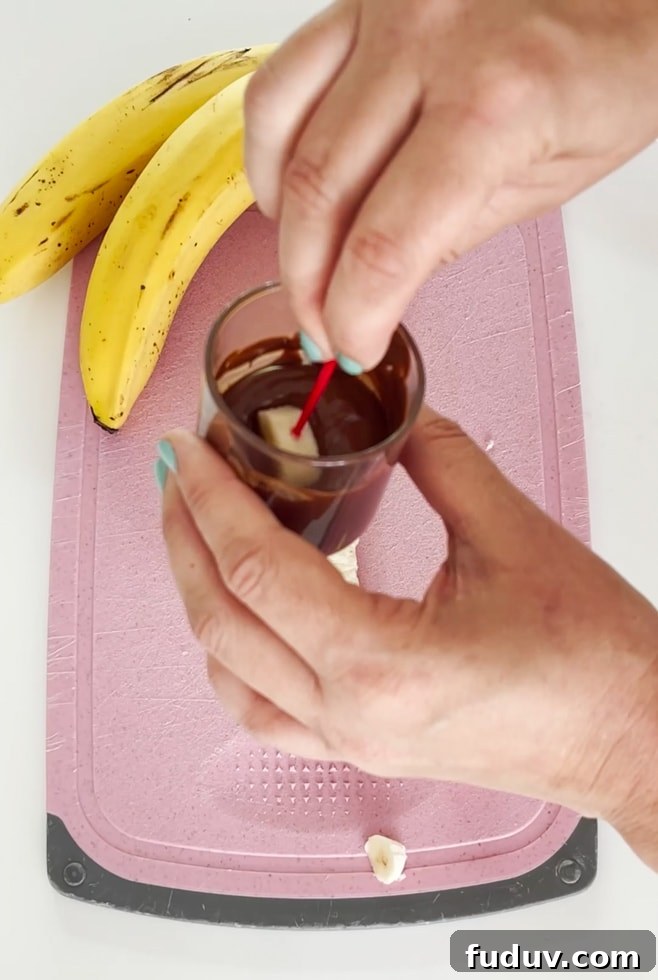 Banana slice being dipped into a small pot of melted mil chocolate.