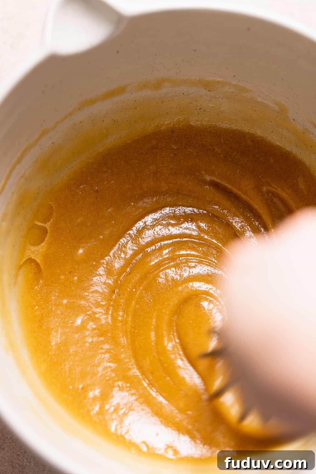 A whisk mixing the eggs into the butter and sugar mixture.