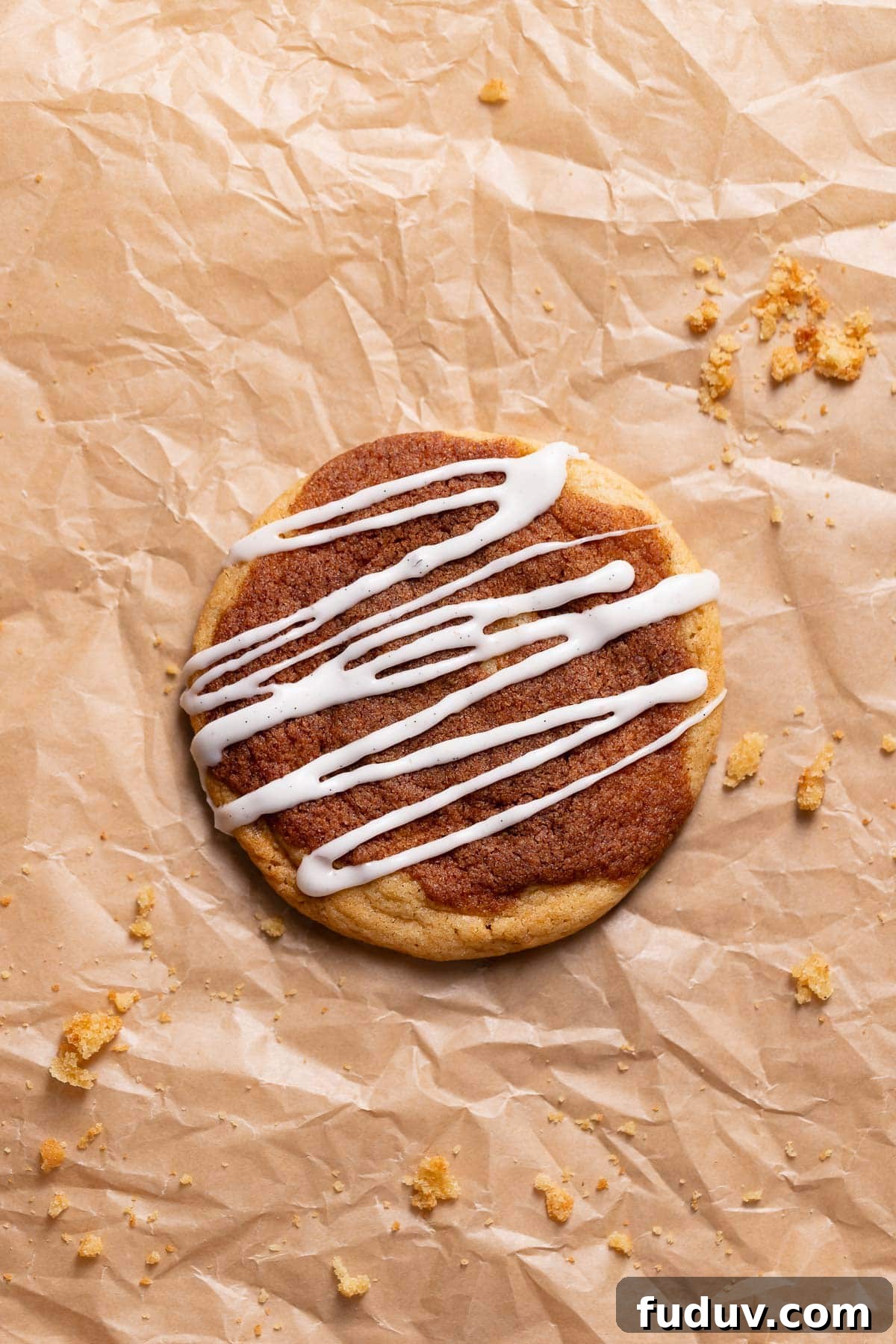 A cinnamon roll cookie on parchment paper drizzled with cream cheese icing.