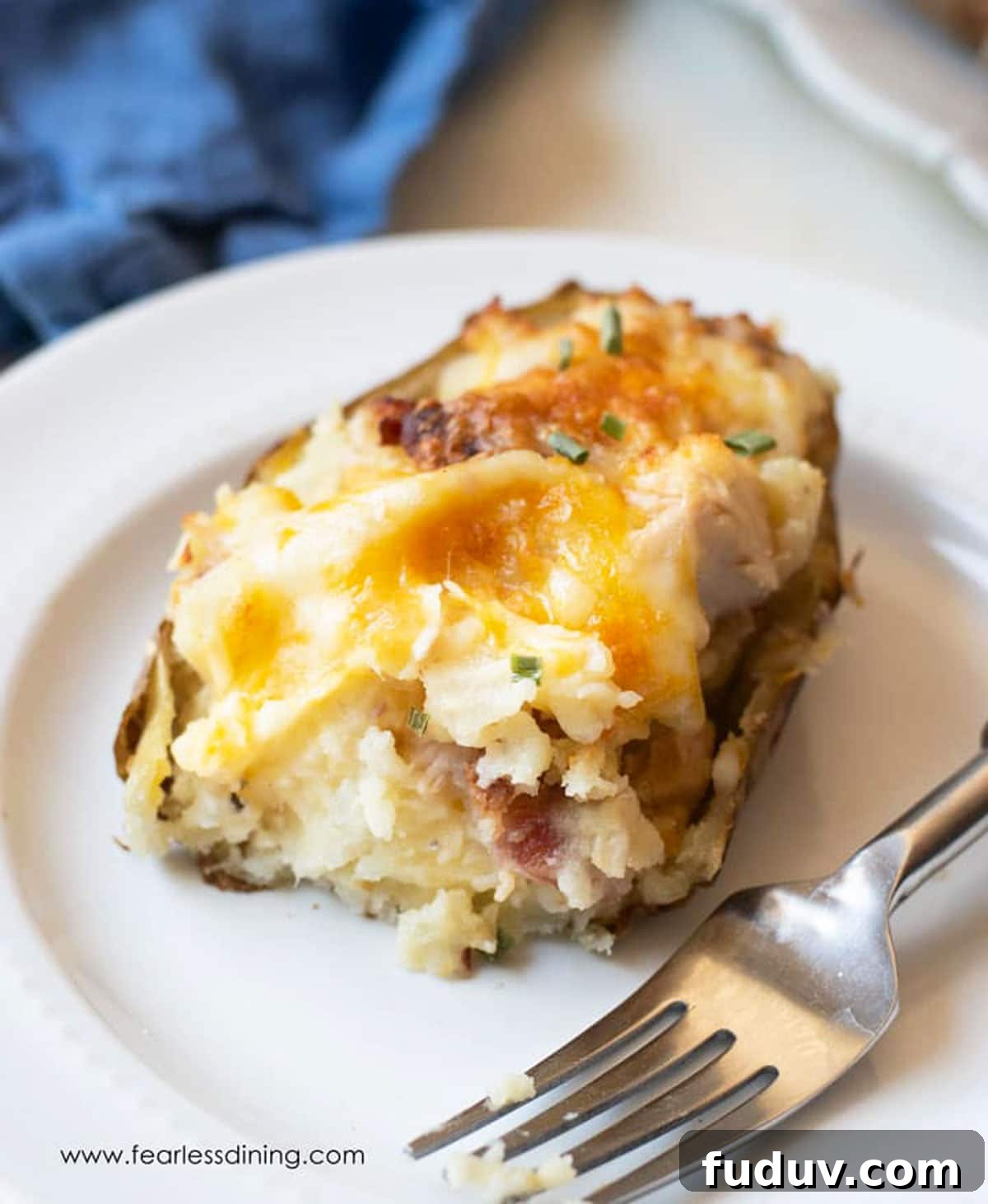 Air Fryer Twice-Baked Potatoes with Chicken and Crispy Bacon 7 A twice baked potato on a white plate. A bite is missing from the potato.