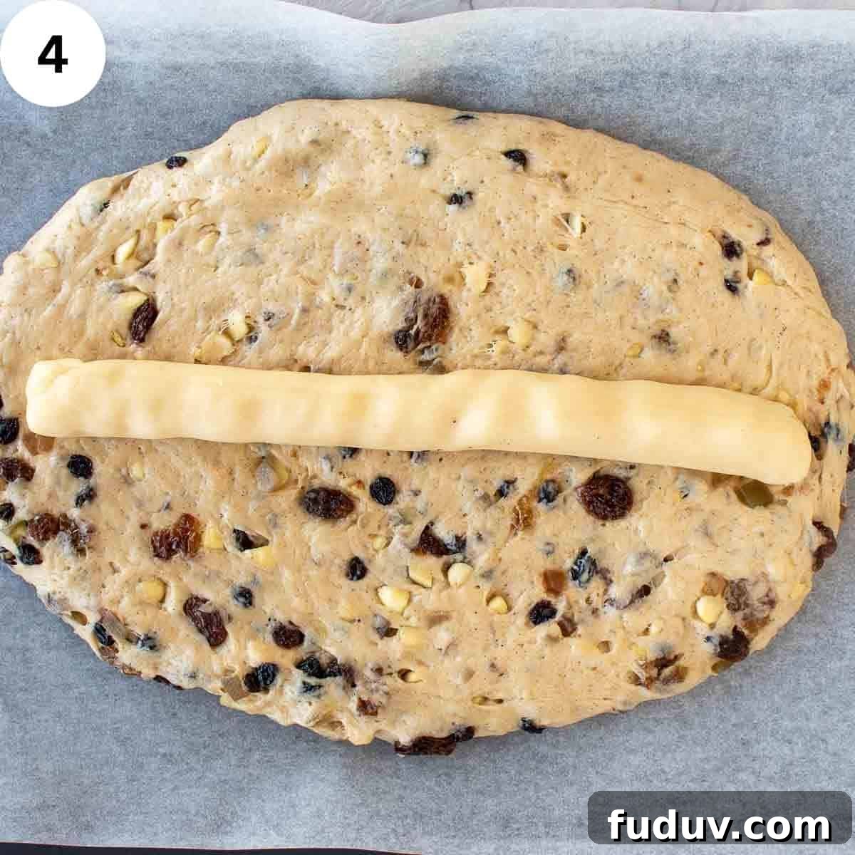 Traditional German Stollen Recipe: Classic Holiday Fruit Bread 7 Dough with dried fruit through it, in a flat oval shape with a long log of marzipan on top.