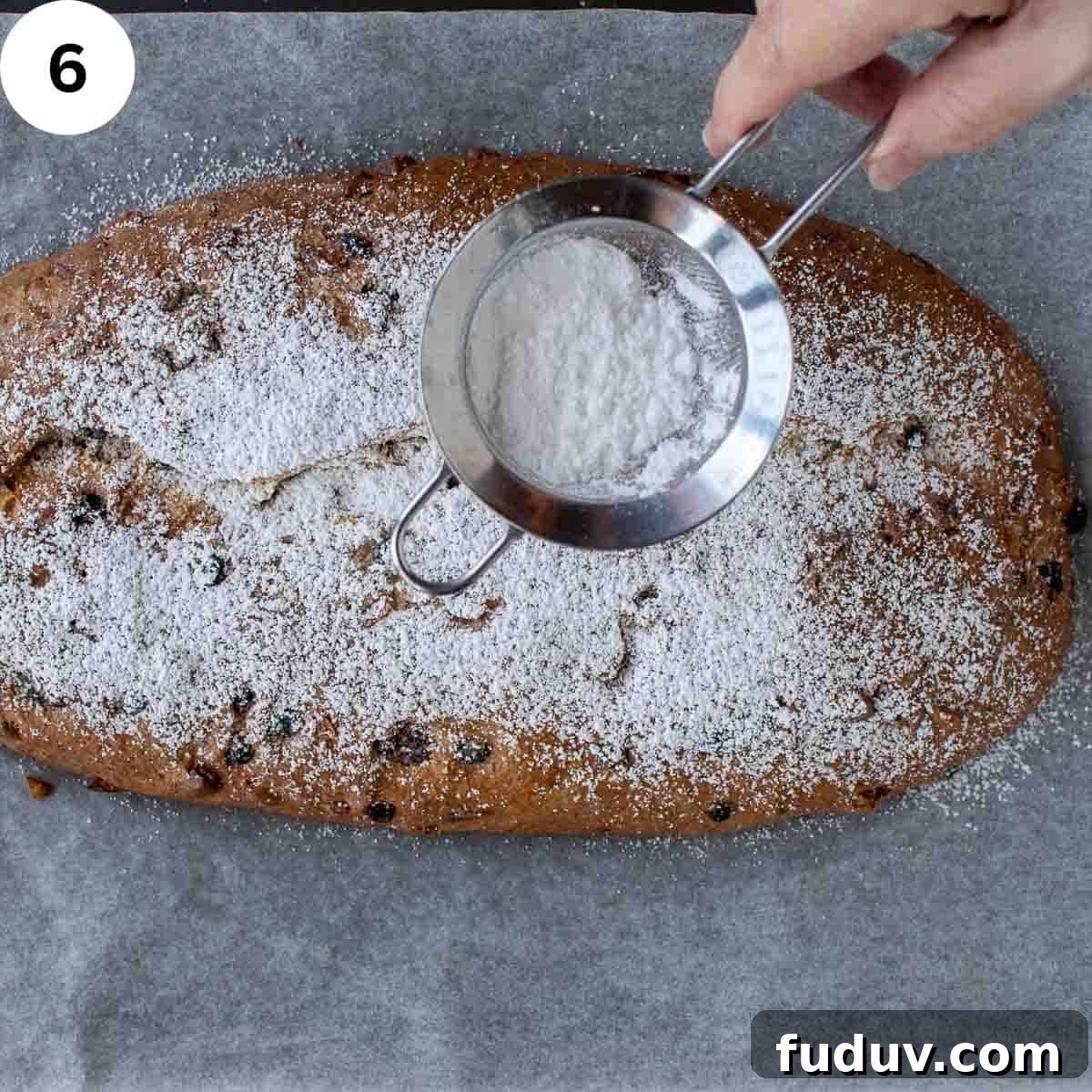 Traditional German Stollen Recipe: Classic Holiday Fruit Bread 9 Powdered sugar being dusted over fruited baked bread.
