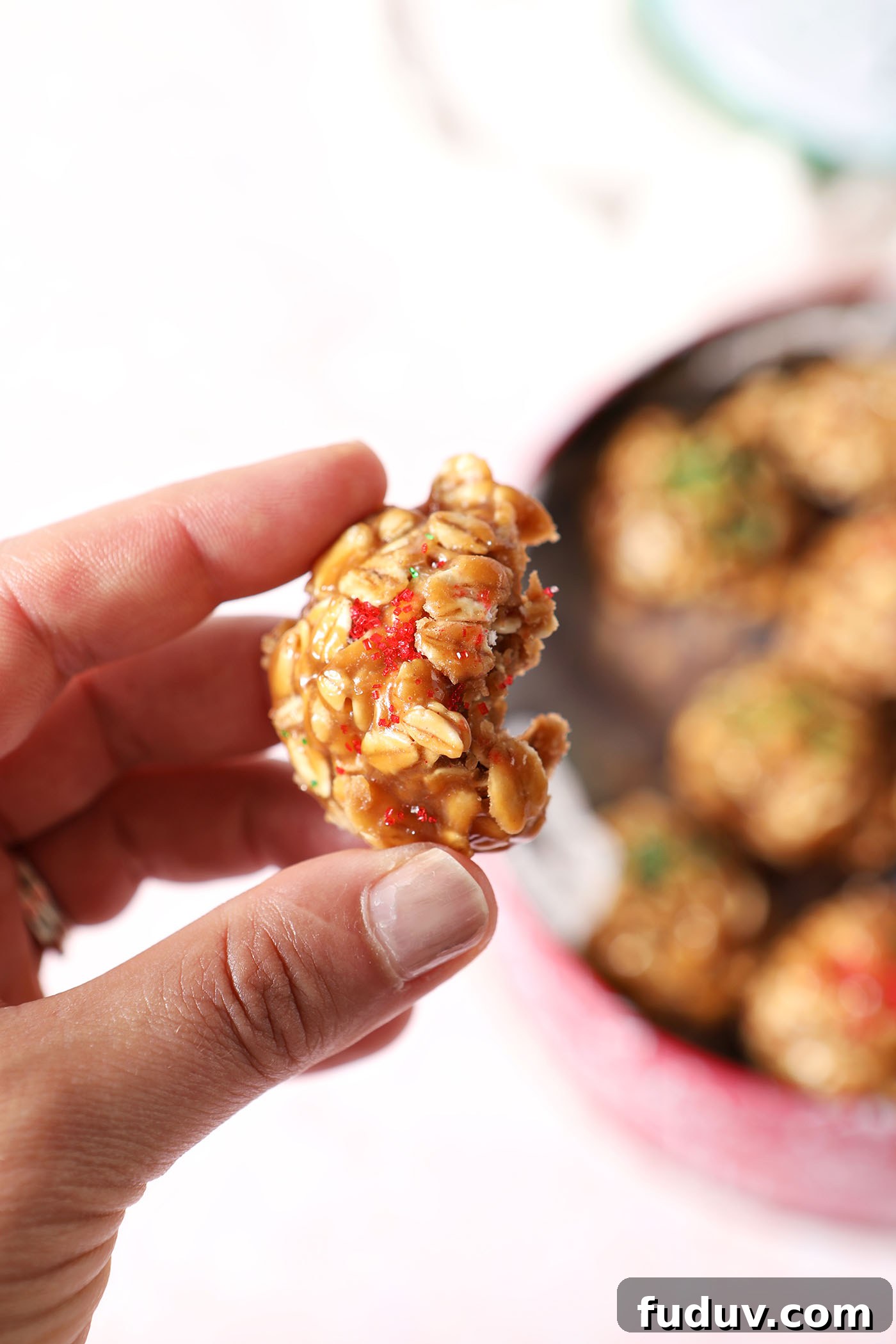 A hand holds a bitten-into no bake cookie above a cookie tin of more