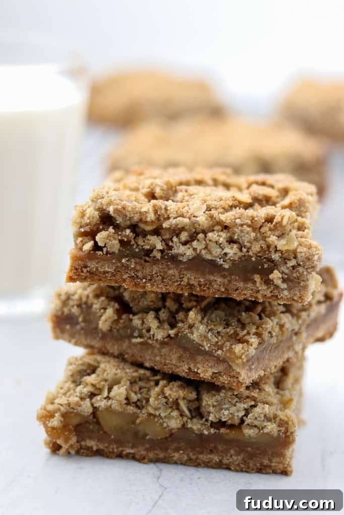 A close up of a stack of apple crumble bars with a glass of milk