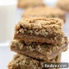 A close up of a stack of apple crumble bars with a glass of milk