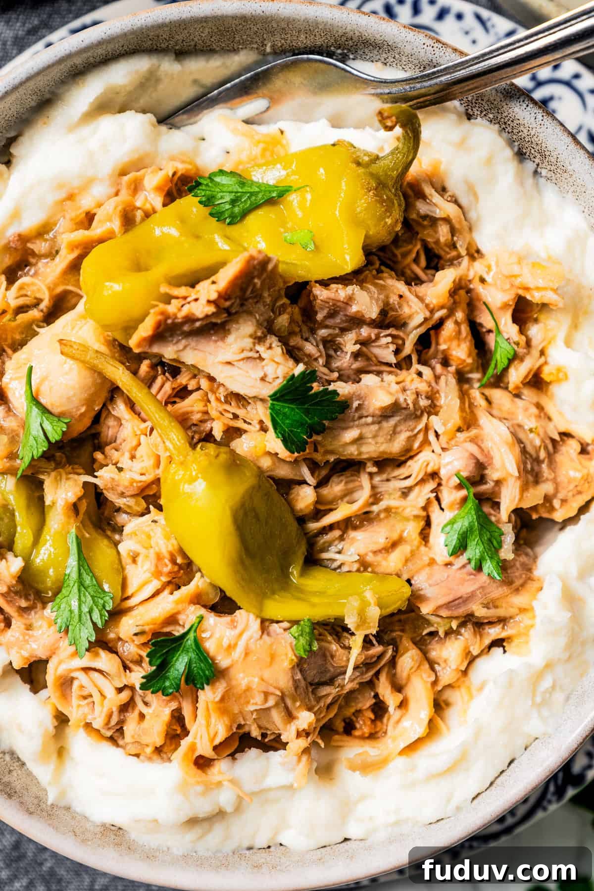 Mississippi chicken is an easy crock pot recipe with juicy chicken shredded in savory pepperoncini ranch sauce. Make it with 5 ingredients! Close-up photo of shredded Mississippi chicken and pepperoncini served over mashed potatoes.